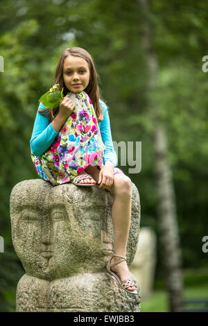 Niedliche kleine Mädchen sitzt auf einem Stein Totem im Park. Stockfoto