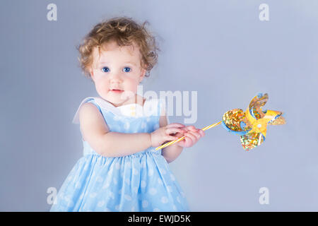 Schönes kleines Mädchen spielen mit einem Wind-Spielzeug auf hellblauem Hintergrund Stockfoto