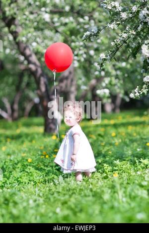 Lustige Babymädchen spielen mit einem großen roten Ballon Stockfoto