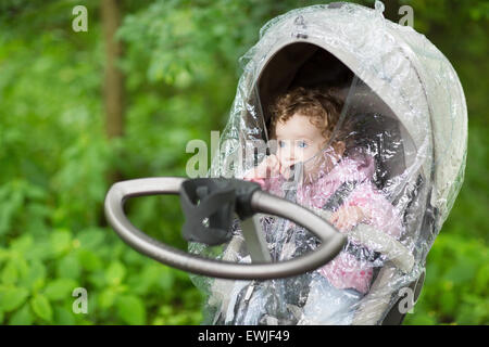 Kleines Mädchen sitzt in einem Kinderwagen unter einem Regenschutz an einem kalten und regnerischen Herbsttag Stockfoto