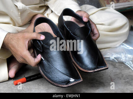 Peshawar. 27. Juni 2015. Ein pakistanischer Mann zeigt ein paar traditionelle Peshawari Chappal bei einem Workshop in Nordwest-Pakistan Peshawar, 27. Juni 2015. Peshawari Chappal ist ein traditionelles Schuhwerk von Pakistan, getragen vor allem von Paschtunen Khyber Pakhtunkhwa Region von Pakistan. © Ahmad Sidique/Xinhua/Alamy Live-Nachrichten Stockfoto