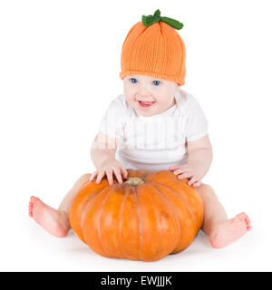 Lustig Lachen kleines Baby sitzen und spielen auf einen riesigen Kürbis einen gestrickten Kürbis Hut auf weißem Hintergrund Stockfoto