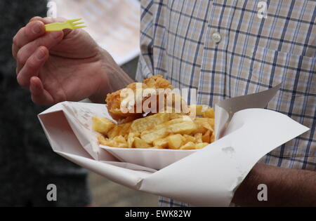 Ein Mann isst Fisch und Chips aus einem Fach im freien - Sommer, England UK Stockfoto