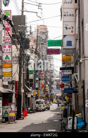 Typische japanische Stadt Straße. Schmale Straße zwischen zwei Reihen von Geschäften, Läden und Häuser mit Overhead Zeichen, Kabel und Drähte durcheinandergeworfen. Stockfoto