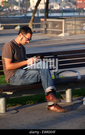 Junger Mann sitzen auf Bank mit Mobile/Handy Stockfoto