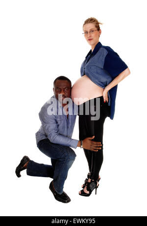 Ein afrikanischer amerikanischer Mann kniend vor seine kaukasischen Frau hört auf den Babybauch, weißen Hintergrund isoliert. Stockfoto