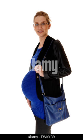 Eine schwangere Frau in einem blauen Kleid und schwarzen Mantel und Geldbörse stehen im Profil, für weißen Hintergrund isoliert. Stockfoto