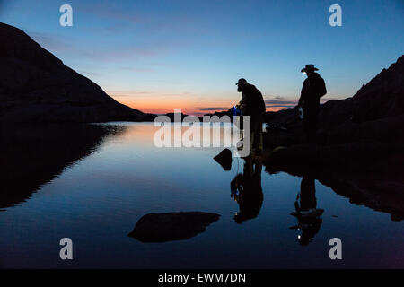 Drei Wanderer füllen Wasserflaschen in der Morgendämmerung mit Reflexionen über Lake Trail auf dem Mt. Whitney Trail. Stockfoto