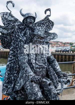 Ein Mann posiert als eine sehr aufwendige lebende Statue auf einem Dreirad und mit einem Teufel auf dem Rücken in Whitby North Yorkshire England UK Stockfoto