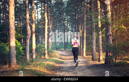 Junge Frau läuft auf einer Landstraße bei Sonnenuntergang in Sommerwiese. Lifestyle-Sport-Hintergrund Stockfoto