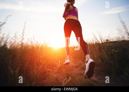 Junge Frau läuft auf einer Landstraße bei Sonnenuntergang in Sommerwiese. Lifestyle-Sport-Hintergrund