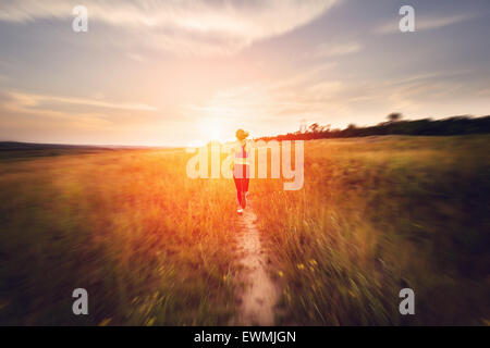 Junge Frau läuft auf einer Landstraße bei Sonnenuntergang in Sommerwiese. Lifestyle-Sport-Hintergrund Stockfoto
