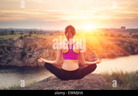 Junge Frau praktizieren Yoga auf dem Hügel bei Sonnenuntergang in der Nähe des Flusses. Stockfoto