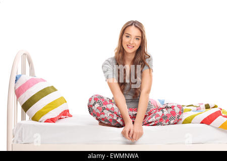 Schöne Brünette Frau sitzt auf einem Bett in ihrem Pyjama und schaut in die Kamera, die isoliert auf weißem Hintergrund Stockfoto