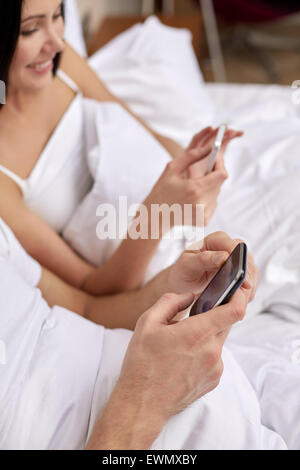 Nahaufnahme eines lächelnden paar im Bett mit smartphones Stockfoto