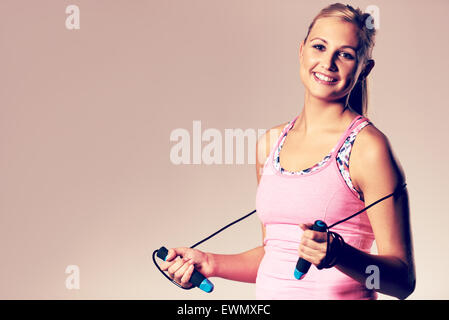 Junge Frau in sportklamotten an Kamera hält ein Seil springen lächelnd. Stockfoto