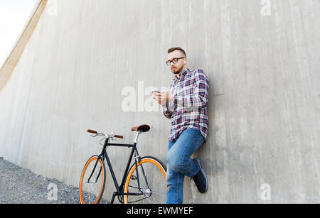 Hipster-Mann im Ohrhörer mit Smartphone und Fahrrad Stockfoto