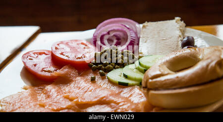 Schöne Platte Räucherlachs und Bagel mit Beilagen hinterleuchtet Fensterlicht Stockfoto