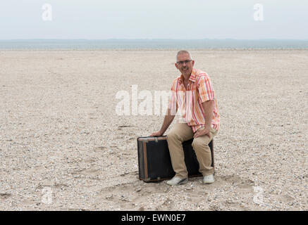 Mann mit alten Koffer am Strand sitzen Reisen Stockfoto