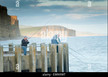 Fischer am Ende von einer Anlegestelle in West Bay, in der Nähe von Bridport in der Grafschaft Dorset, England mit der Jurassic Küste hinter. Stockfoto