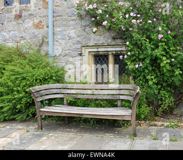 Sitzbank in einem englischen mittelalterlichen Garten mit Rosen, die Kletterwand hinter Stockfoto