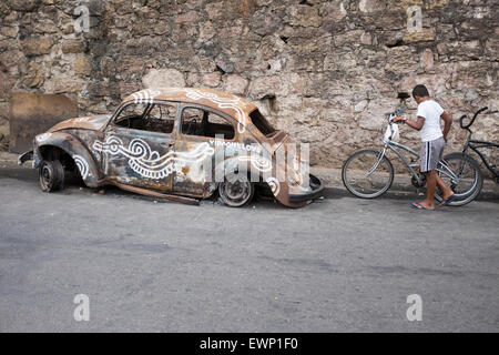 RIO DE JANEIRO, Brasilien - 7. März 2015: Brasilianische Mann schiebt Fahrrad vorbei verwüstet Fusca Auto in der Favela Vidigal. Stockfoto