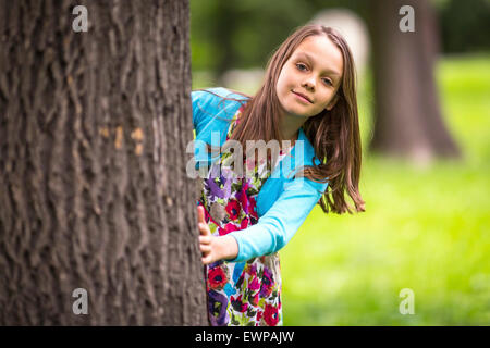 Niedliche kleine Mädchen spähen hinter einem Baum. Stockfoto