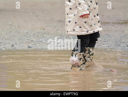 junge Mädchen tragen geblüht Gummistiefel zu Fuß durch schlammige Pfütze Stockfoto