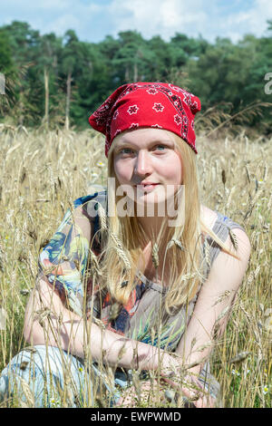 Blonde kaukasische Teenager-Mädchen sitzen im Kornfeld tragen rote Taschentuch Stockfoto