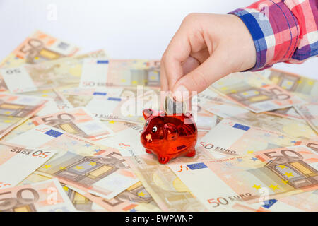 Hand des Kindes aufsetzen viele Ausbreitung Euro-Banknoten-Euro-Münze in roten Sparschwein Stockfoto