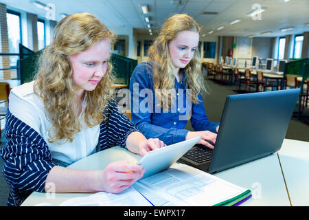 Zwei kaukasischen Schwestern mit langen Haaren, die Arbeiten am Computer und Tablet Computer Unterricht Stockfoto