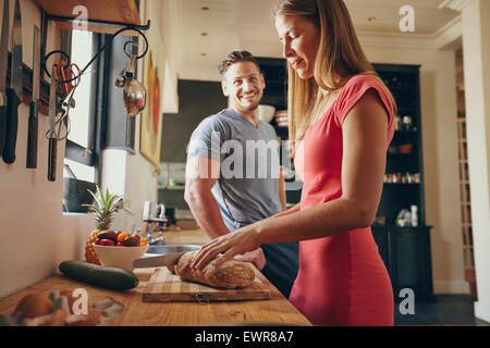 Innenaufnahme der junge Mann und Frau in der Küche am Morgen. Konzentrieren Sie sich auf Frau Schneiden von Brot, das Frühstück zubereitet. Stockfoto
