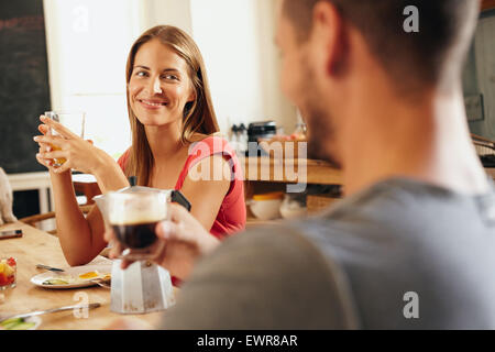 Junges Paar morgens am Frühstückstisch sitzen. Fokus auf junge Frau mit Glas Fruchtsaft und Mann ist unscharf in Stockfoto