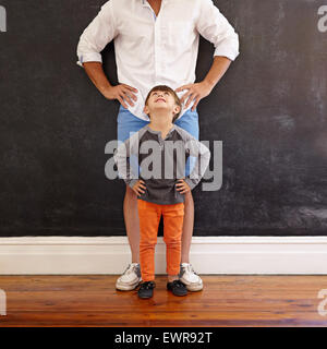 Innenaufnahme des kleinen Jungen Blick auf seinen Vater beim stehen vorne mit den Händen auf Taille. Stockfoto