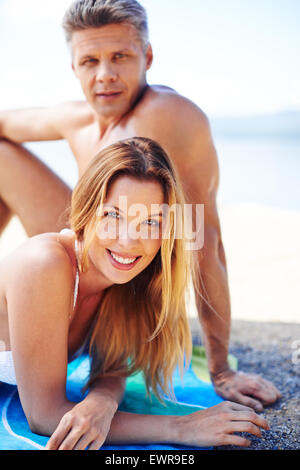 Glückliche junge Sonnenanbeter in Bikini Blick in die Kamera mit erholsamen Mann im Hintergrund Stockfoto