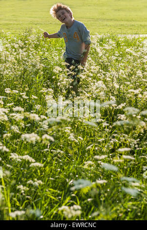 Ein sehr fröhlicher Junge läuft durch eine Wiese Kuh Petersilie und langes Gras im Sommer mit der Sonne glänzend und sehr glücklich Stockfoto