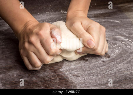 Backen, Vorbereitung Hintergrunds. Weibliche Hände kneten den Teig auf der Arbeitsplatte. Stockfoto