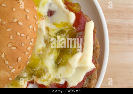 Enge Draufsicht einen Cheeseburger in einem Sesam Brötchen bedeckt mit Mayonnaise, Ketchup und lustvoll auf einen kleinen Teller oben auf der Registerkarte "Holz" Stockfoto