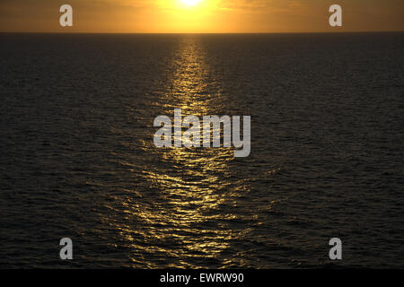 Die untergehende Sonne reflektiert die Wellen über einer Wasserfläche Stockfoto
