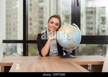Bildnis einer Frau von ihrem Schreibtisch sitzen und halten ein Globe-Modell Stockfoto