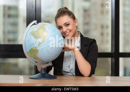 Bildnis einer Frau von ihrem Schreibtisch sitzen und halten ein Globe-Modell Stockfoto