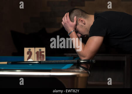 Junger Mann sucht verwirrt am Billard-Tisch - er verliert Stockfoto