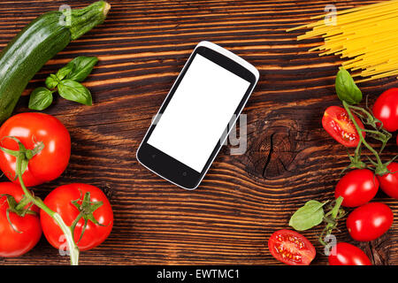 Frisches Gemüse und Nudeln auf Holztisch mit Smartphone und Rezept auf dem Bildschirm. Lebensmittel, Rezepte und kochen. Moderne Küche Stockfoto