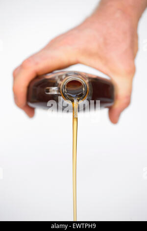 Hand gießen Bio amerikanischer Ahorn Sirup aus einer Flasche vor weißem Hintergrund Stockfoto