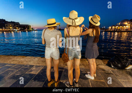 Menschen drei junge Frauen in Strohhüten Chania Hafen Kreta Touristen Griechenland in der Abenddämmerung Kreta Chania Griechenland Rückansicht Sonnenuntergang Landschaft Stockfoto