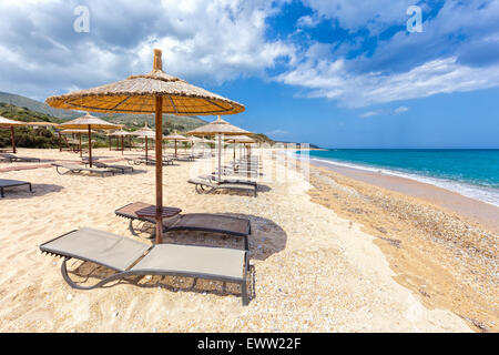 Sonnenschirme in Reihen für Schatten am Sandstrand an der Küste mit blauen Meer in Griechenland Stockfoto