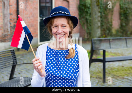 Kaukasische mittlere gealterte Frau gekleidet in blaue Kleidung feiert Tag der Befreiung mit niederländischer Flagge Stockfoto