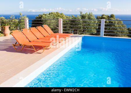 Reihe von orangefarbenen Sonnenliegen zum Entspannen im Urlaub in der Nähe von blauen Swimmingpool Stockfoto