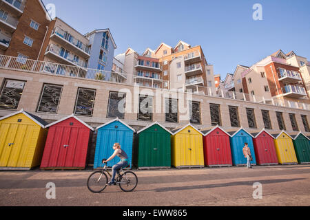 Radfahrer auf dem Fahrrad mit bunten Strandhäuschen und modernen Apartments/Wohnungen am Strand Honeycombe Entwicklung neben Boscombe Rad- Stockfoto