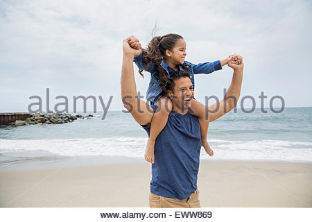 Verspielte Vater Tochter auf den Schultern am Strand tragen